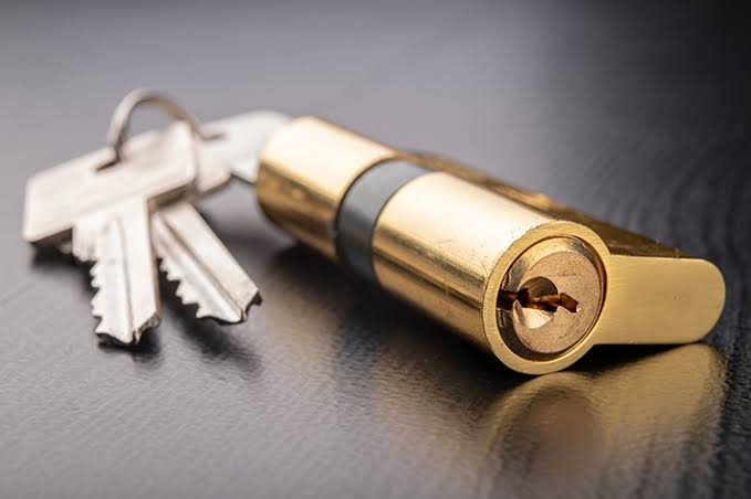 Existing lock cylinder beside a new deadbolt to compare rekeying and replacement