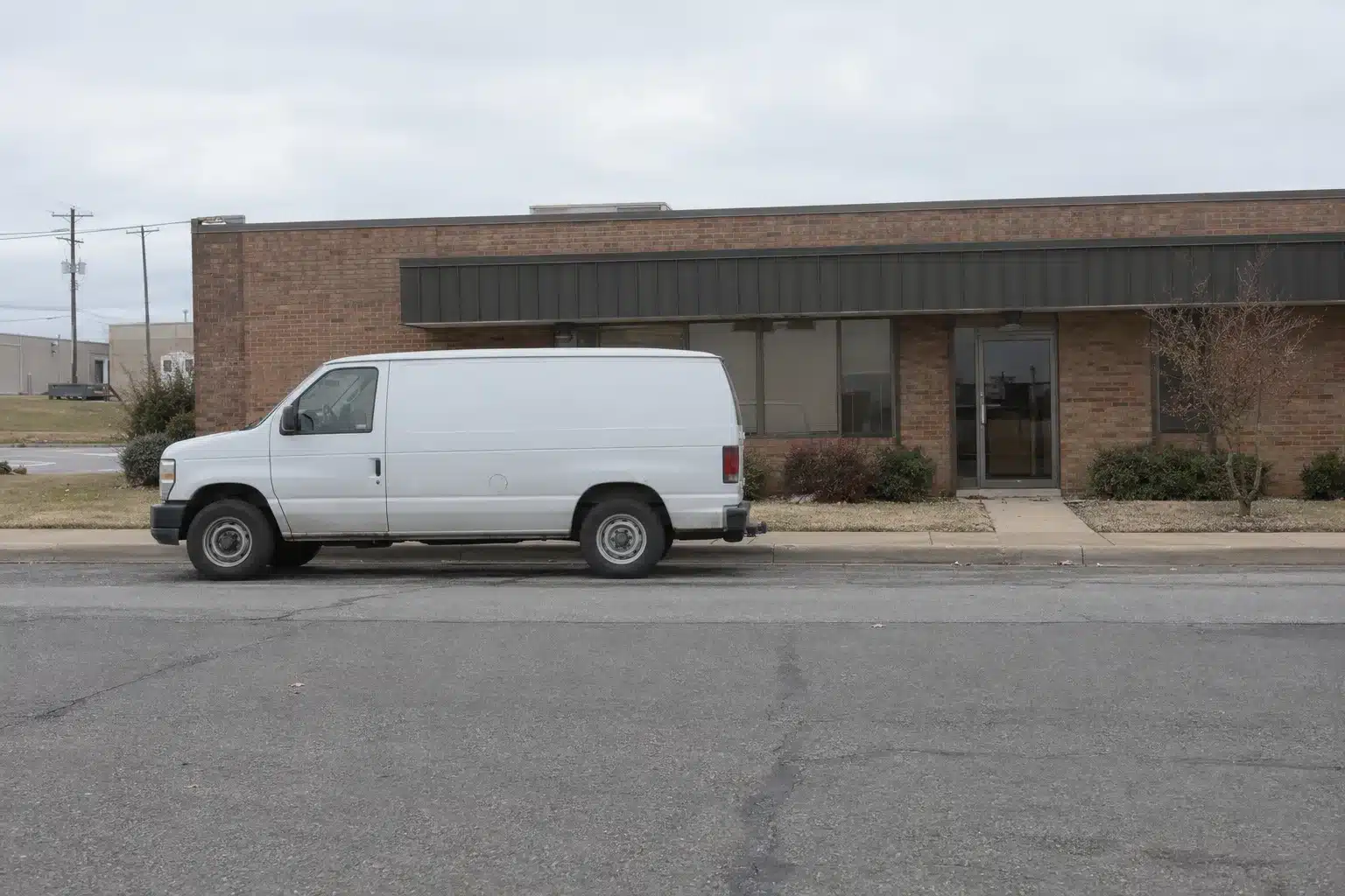 A plain white service van parked in front of a single-story brick commercial building on an Oklahoma City street under overcast morning light